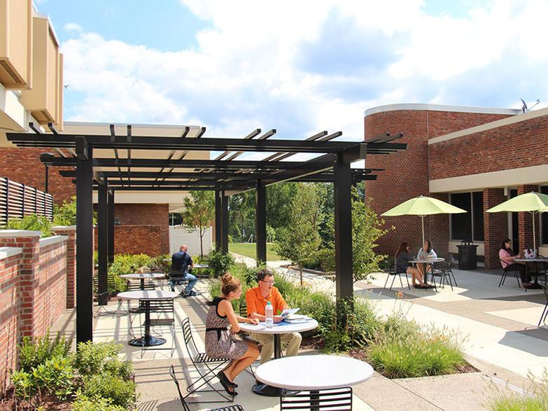 Campus courtyard with students and staff seated around tables and taking in some sun
